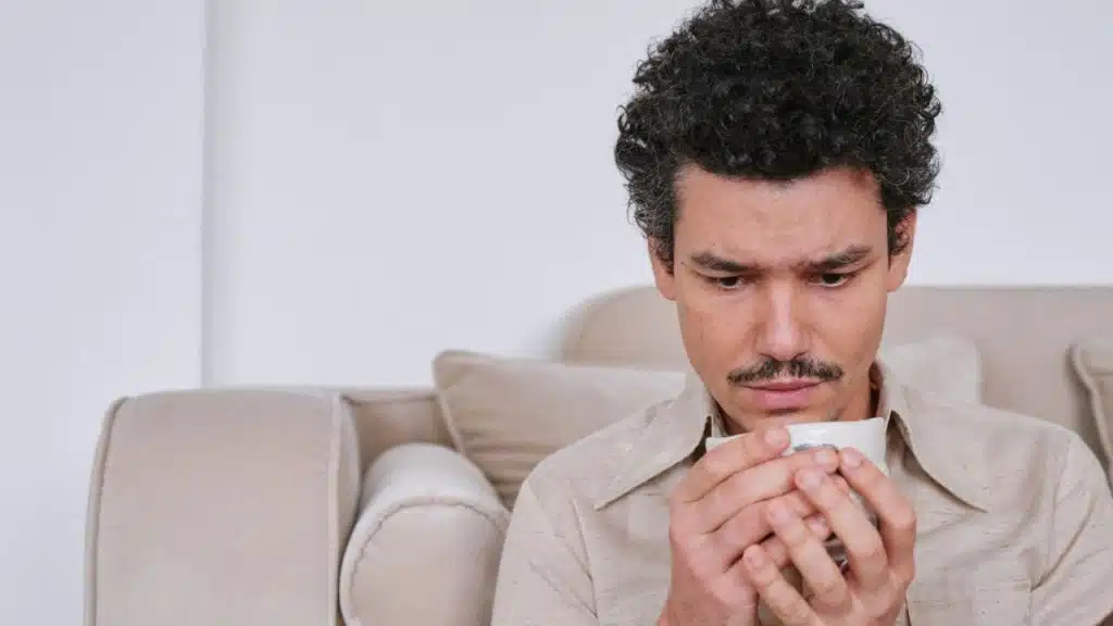 Man with curly hair and a mustache holding a mug, looking down.