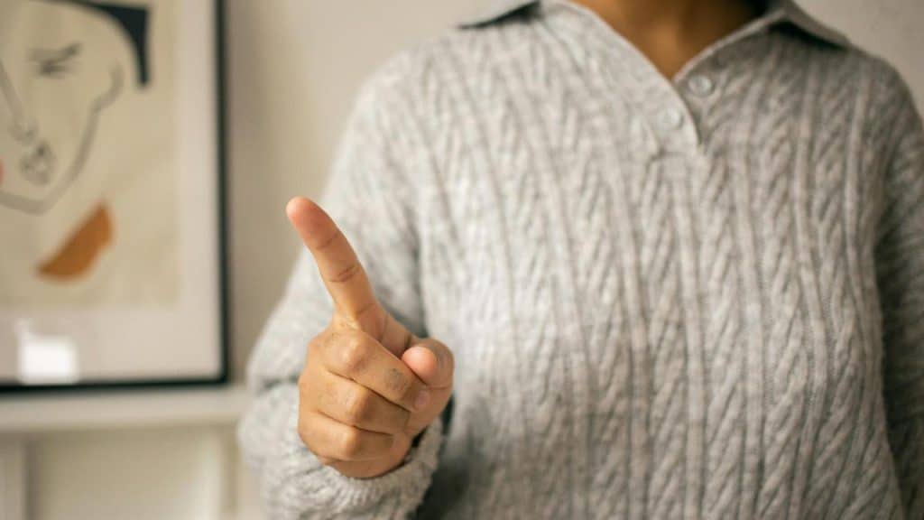 A person pointing their finger while wearing a gray knitted sweater.
