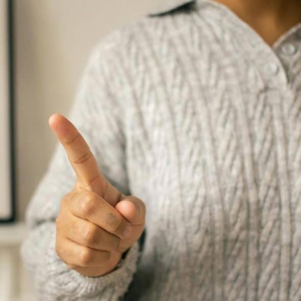 A person pointing their finger while wearing a gray knitted sweater.