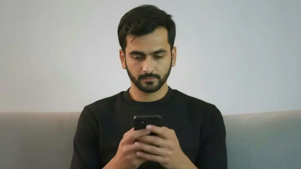 Young man with a beard and black shirt intently looking down at his smartphone.