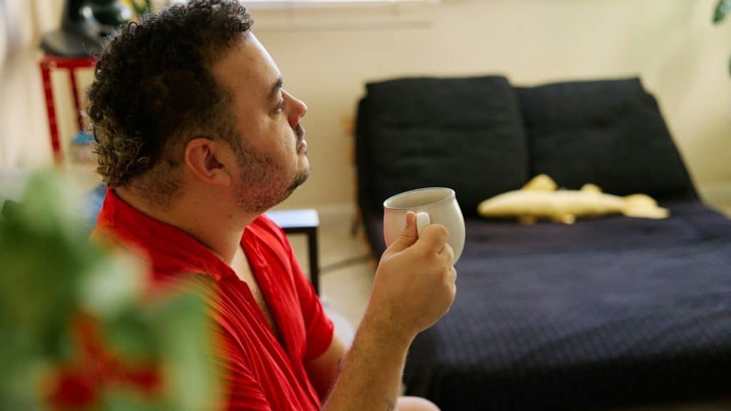 Man in a red shirt holding a mug, looking away in a relaxed indoor setting.