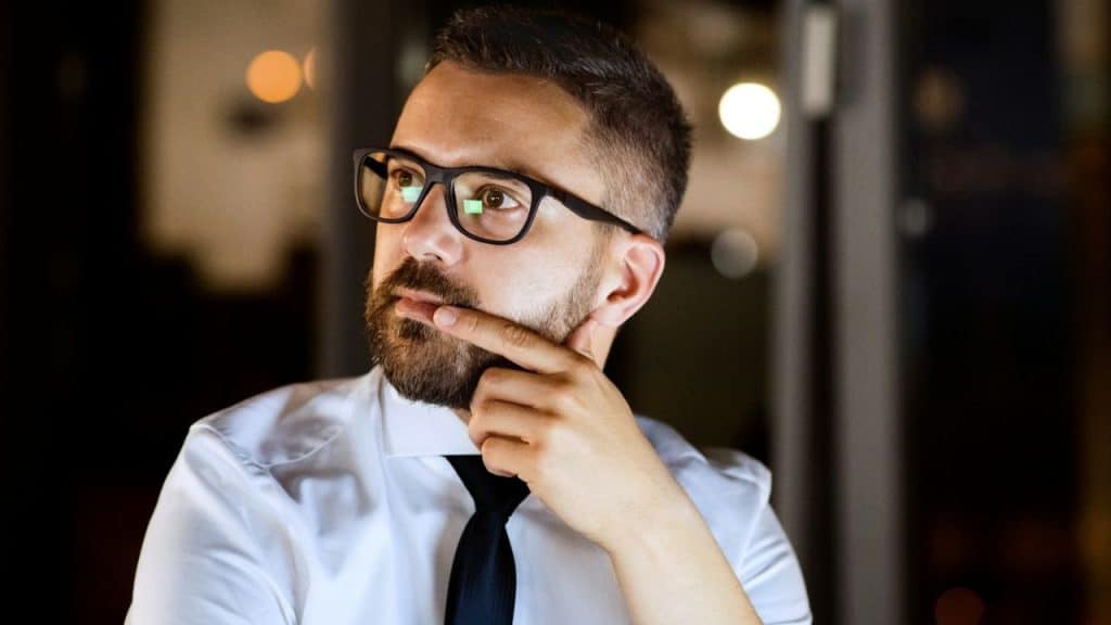 Man in a shirt and tie, wearing glasses, with a thoughtful expression.