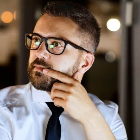 Man in a shirt and tie, wearing glasses, with a thoughtful expression.