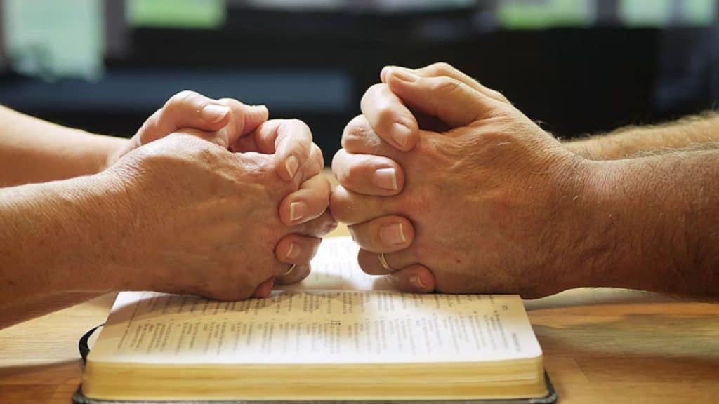 A couple smiling while holding hands in prayer.