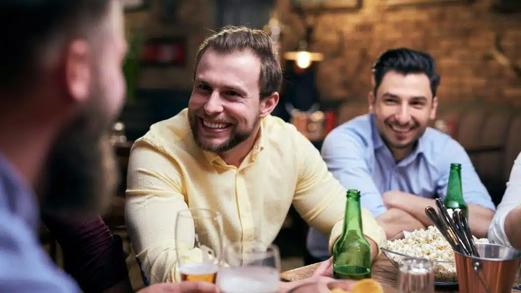 A group of friends laughing and talking at a bar with drinks and popcorn.