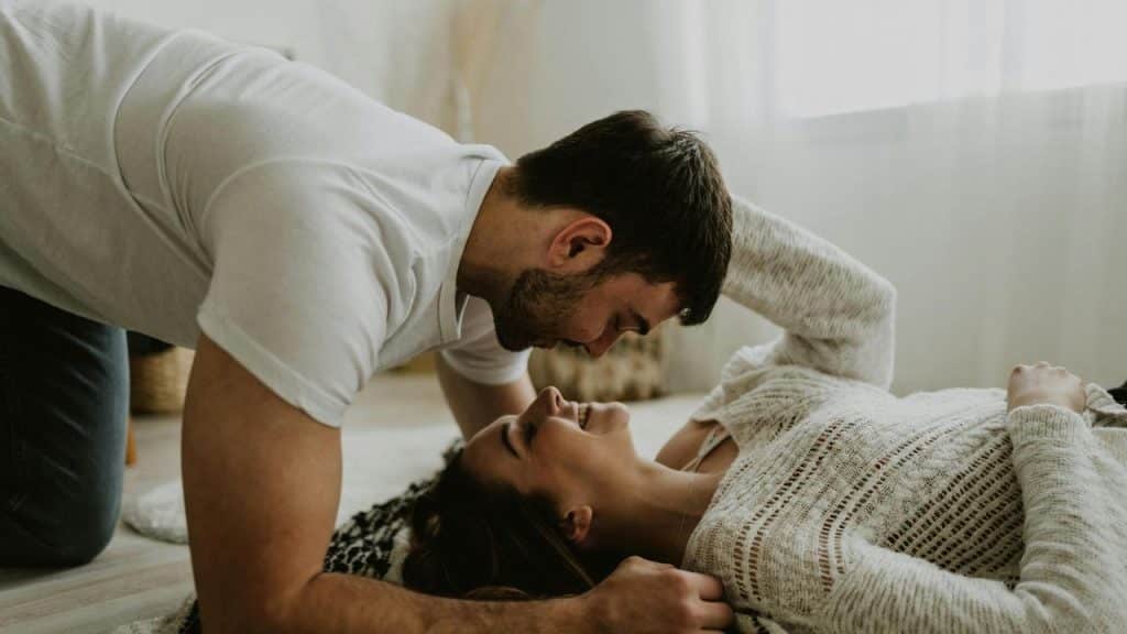 A couple smiling and gazing at each other while lying on the floor.