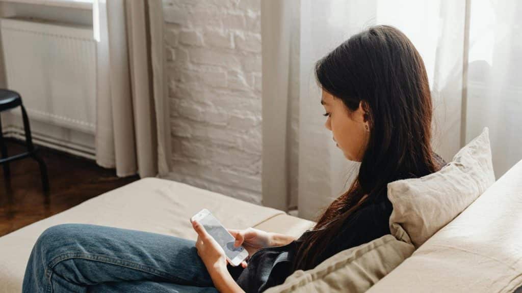 A woman sitting on a couch looking at her smartphone.