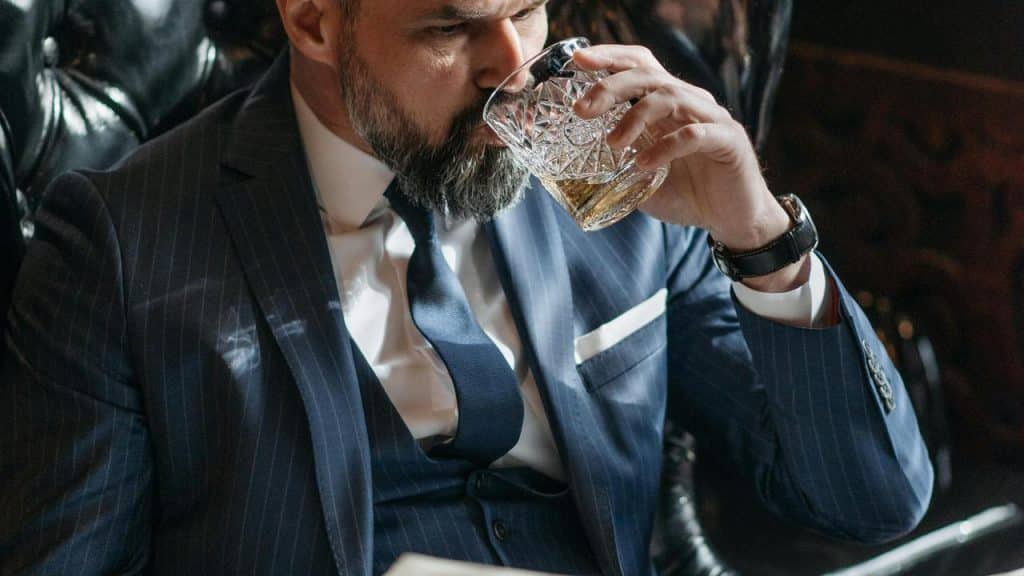 A man in a suit drinking whiskey from a glass.