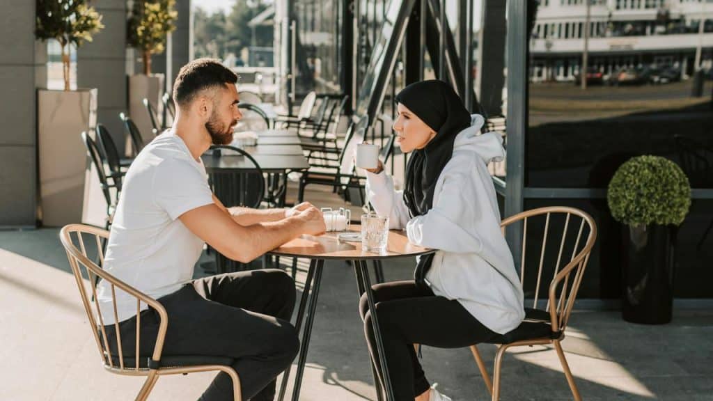A couple sitting at an outdoor café, talking and drinking coffee.