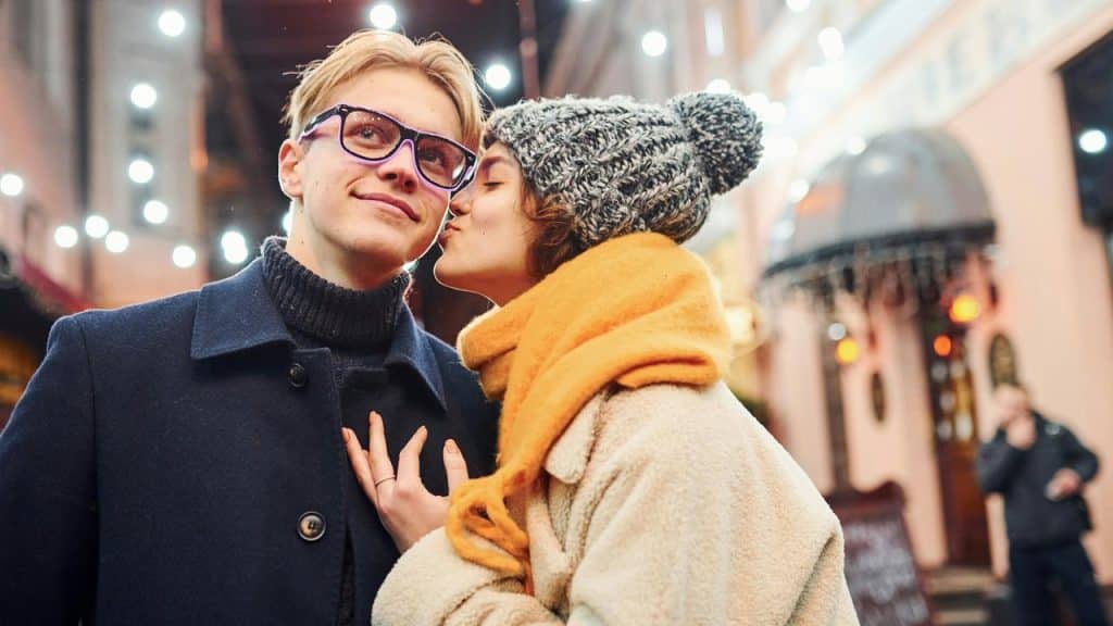 A woman kissing a man’s cheek on a festive street at night.
