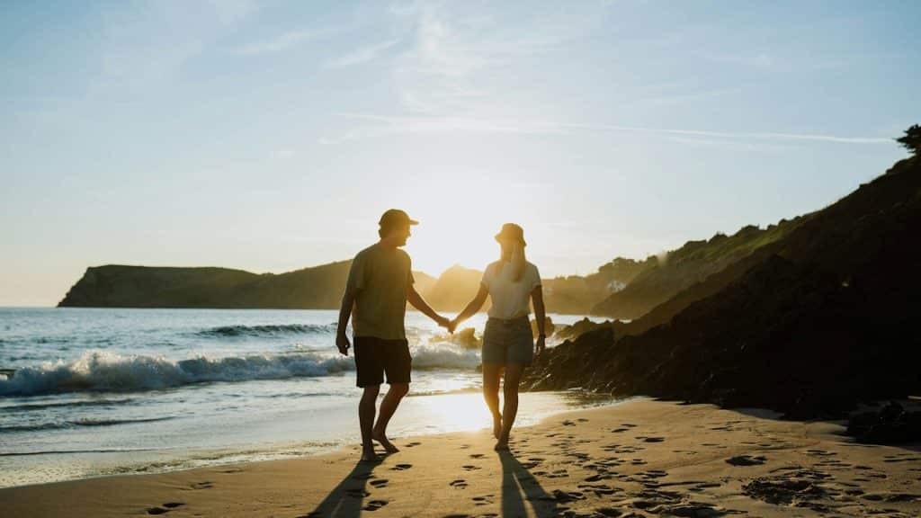 A man and a man walking on a beach holding hands.