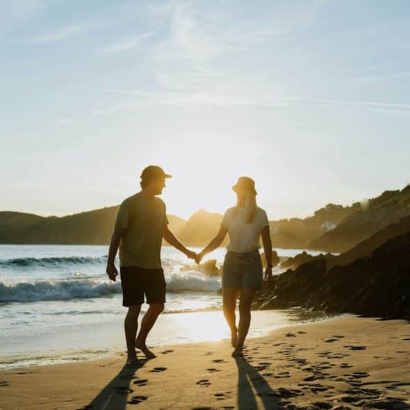 A man and a man walking on a beach holding hands.