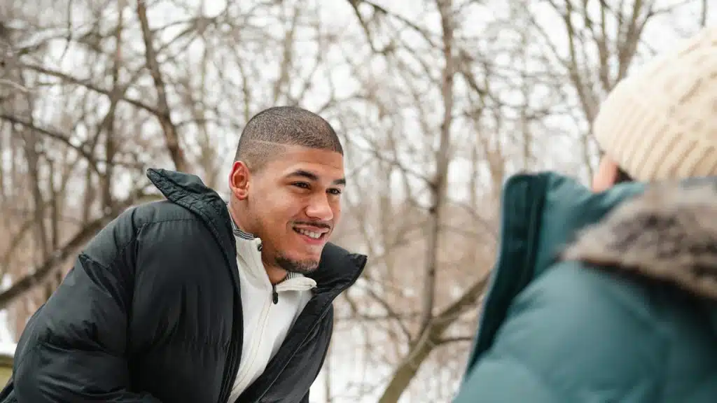 A smiling young man in a black puffer coat looking warmly at a woman.