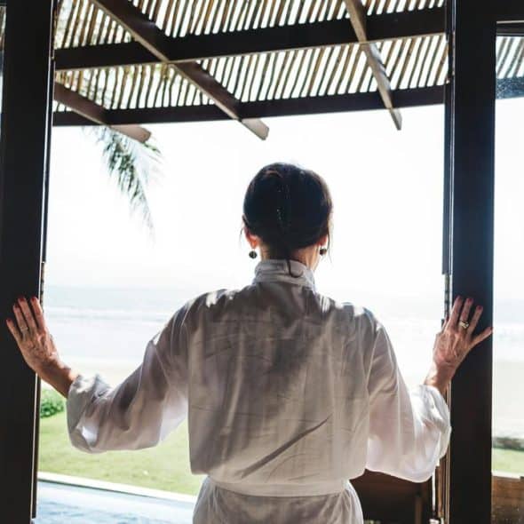 A woman in a robe opens glass doors to a bright beach view.