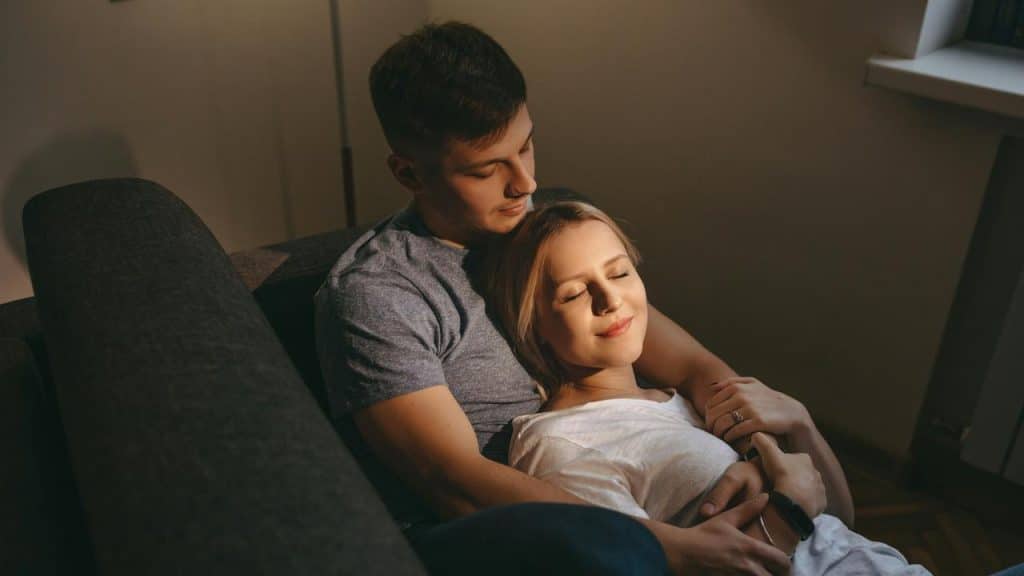 A couple cuddling on a couch, looking relaxed and content.