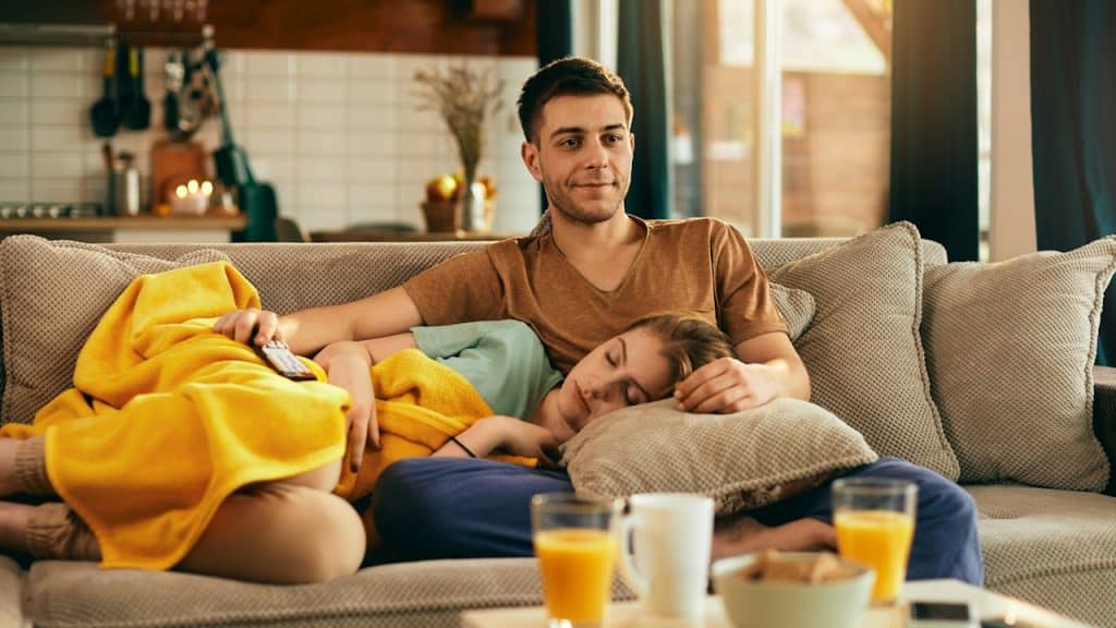 A man watching TV and his partner sleeping on his lap.