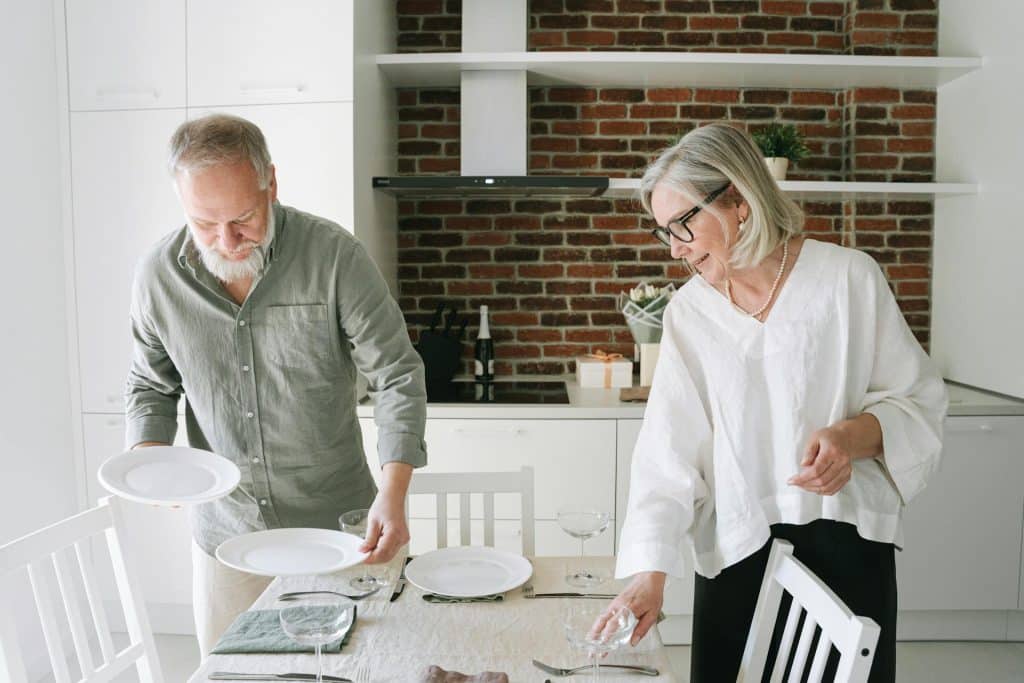 The elderly couple is setting the table together.