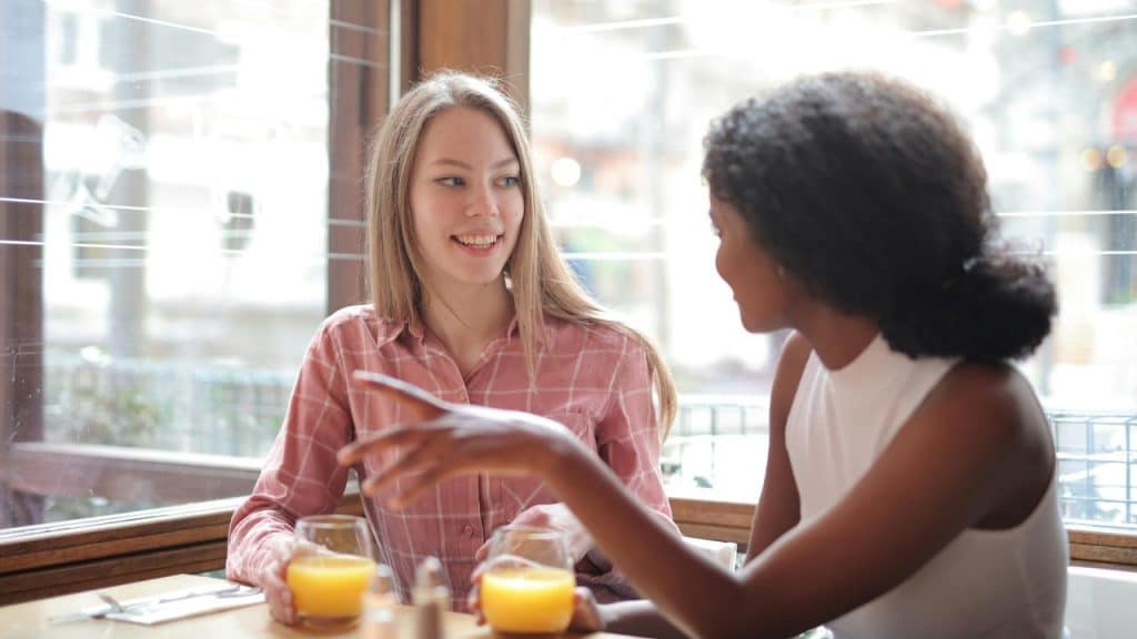 A pair of people talking over drinks at a café table.