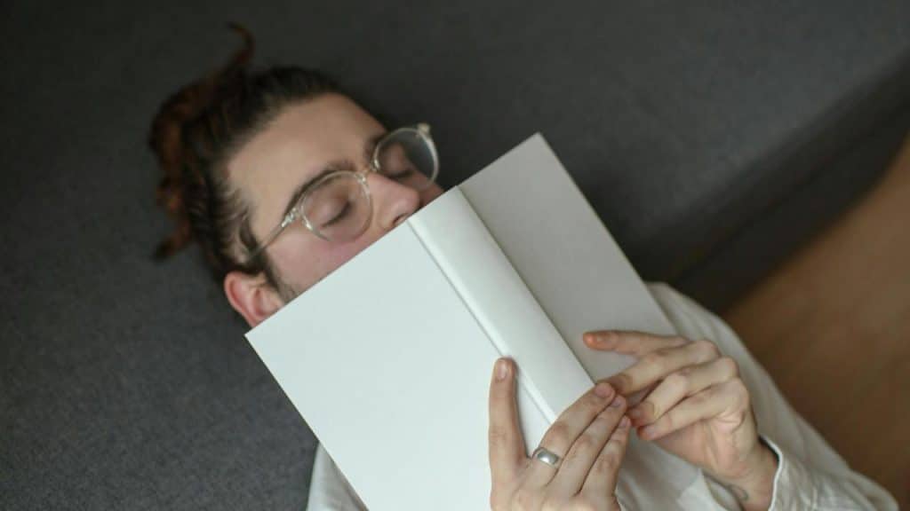 A person lying down with a book covering their face.
