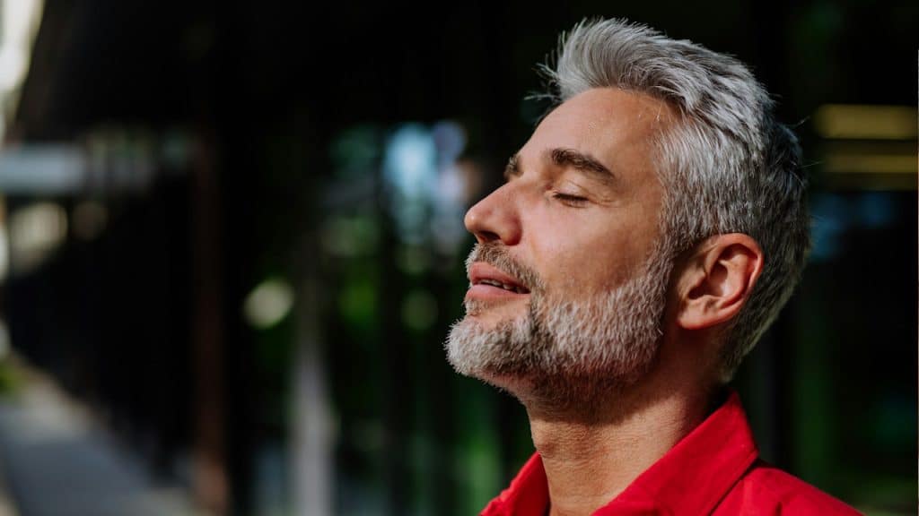 A man with grey hair and a beard looking relaxed with his eyes closed. 