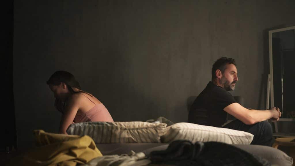 A man and a woman sitting back-to-back in bed.