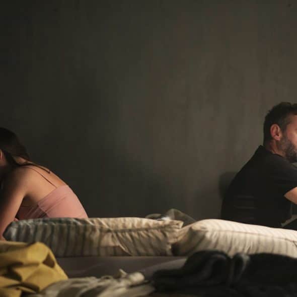 A man and a woman sitting back-to-back in bed.