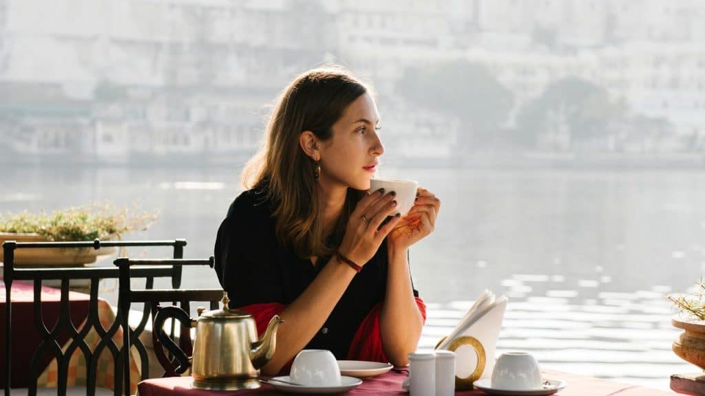 A woman sitting by the water, drinking from a cup at an outdoor café.