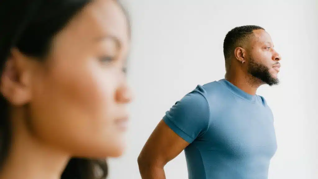 A man in a blue shirt looks to the side, with a blurred woman in the foreground.
