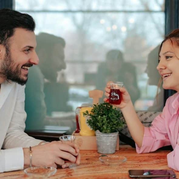 Smiling man and woman seated at a table, drinking from small clear glasses.