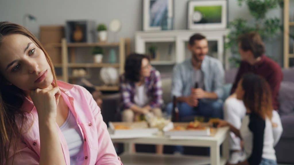 A woman in the foreground looks sad and isolated from a group of friends behind her.