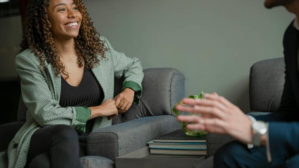 A woman sitting on a chair smiling while talking to someone.