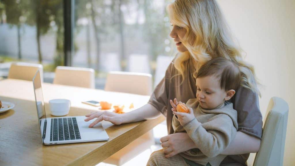 A mother working on a laptop while holding her baby.