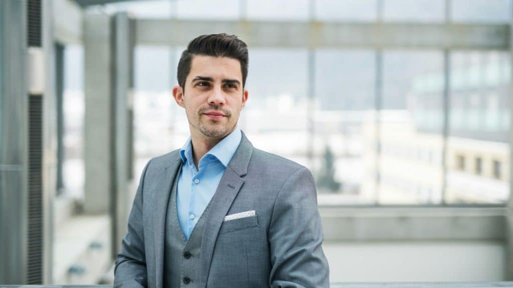 Young man in a gray suit and vest looking off-camera in a modern building.