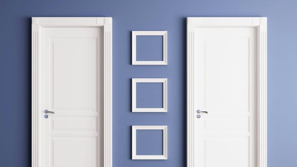 Two white doors with three square picture frames hanging on the wall separating them.
