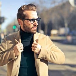 The man is wearing a brown jacket and eyeglasses.