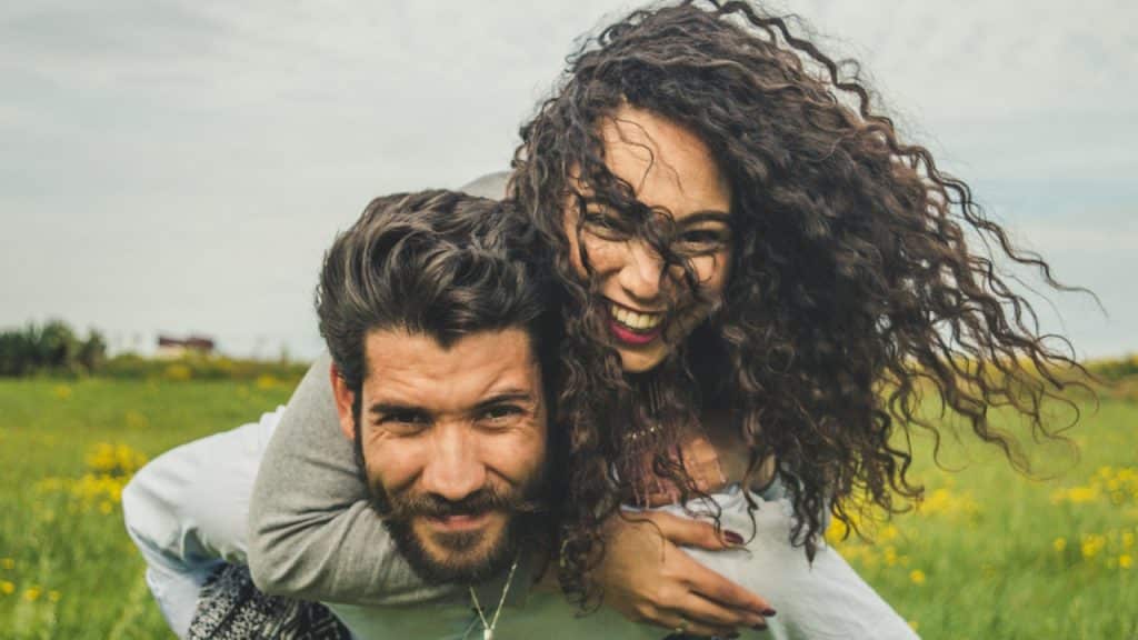 A woman piggybacking on her partner’s back in a field.