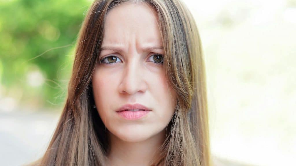 Close-up of a young woman with long brown hair, looking directly at the camera with a worried expression.