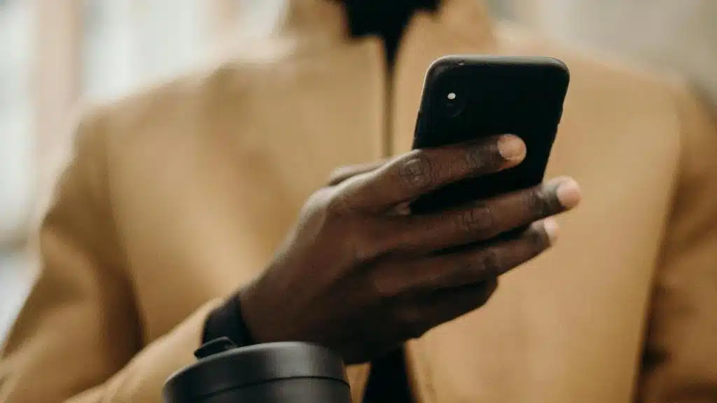 A person holding a smartphone while wearing a beige coat.