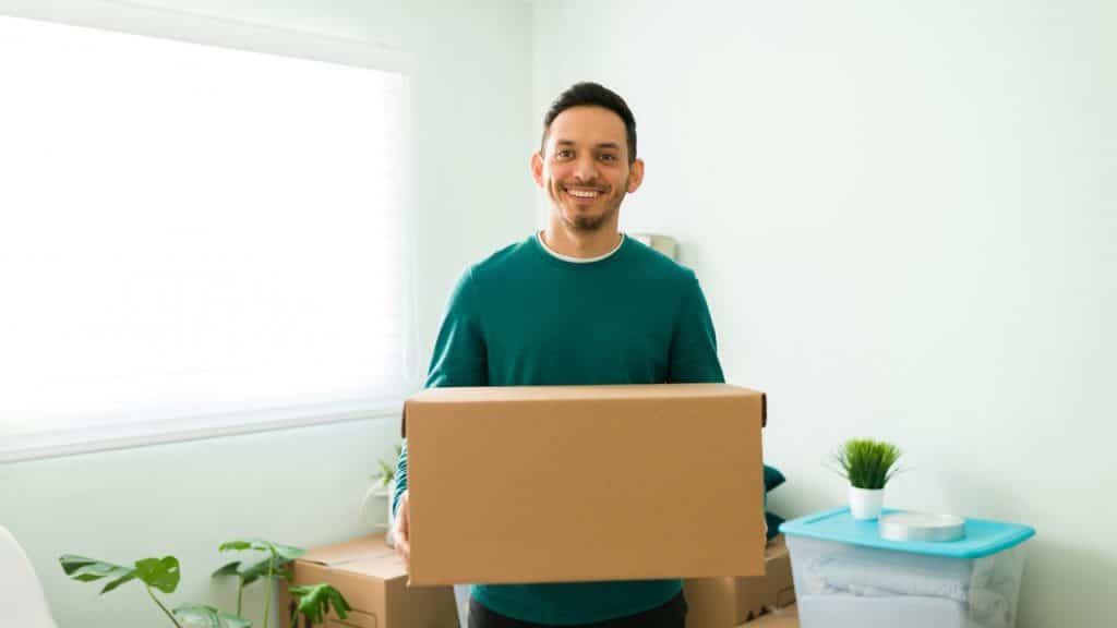 A man carrying a cardboard box and ready to start unpacking the packages in his new home.