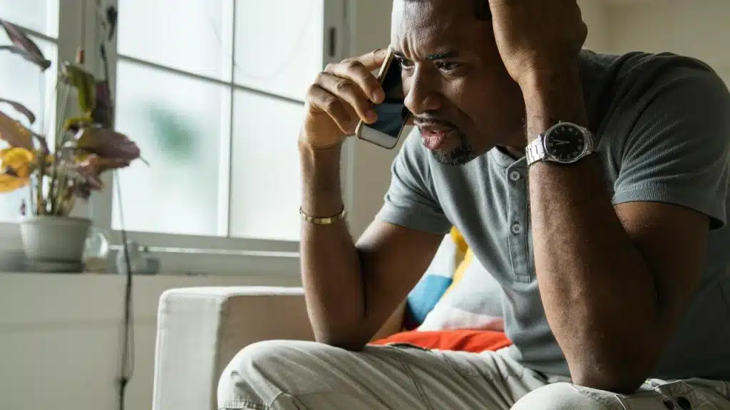 A man sitting on a couch looking worried while talking on the phone.