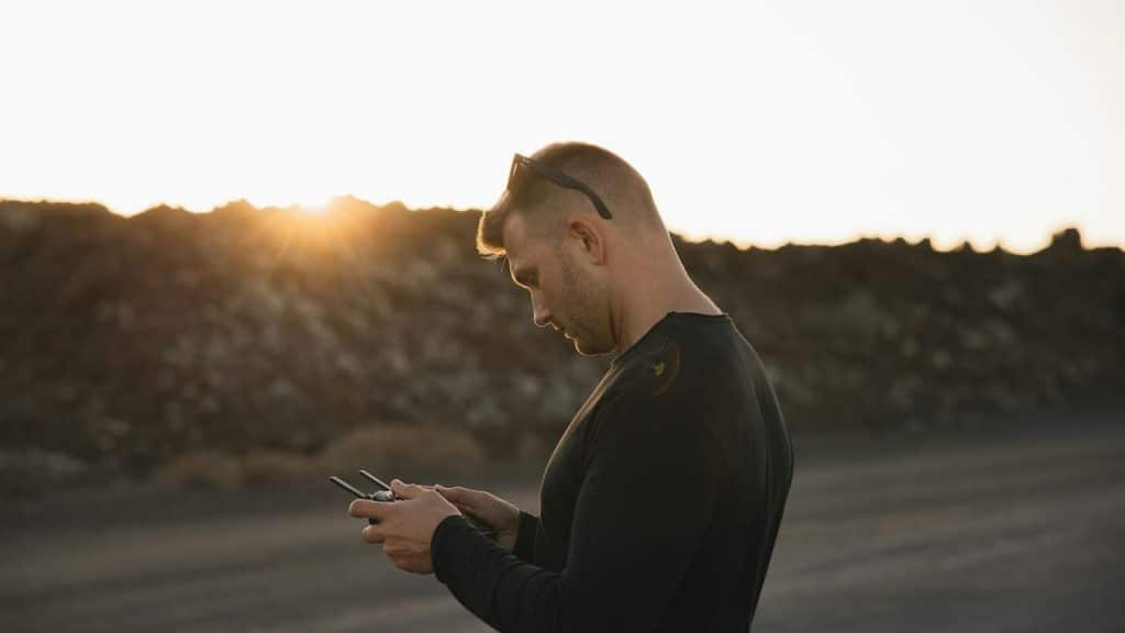 A man using a drone controller outdoors at sunset.
