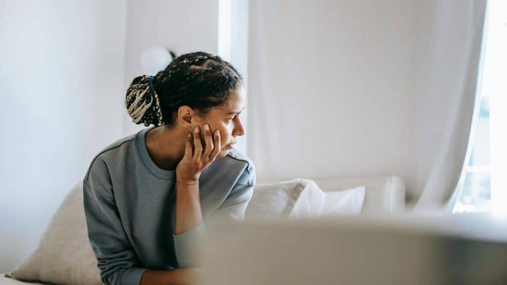 A person sitting on a bed, resting their chin on their hand, appearing pensive.