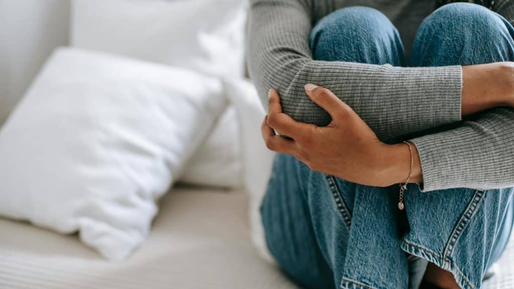 A person sitting on a bed hugging their knees, appearing thoughtful or sad.
