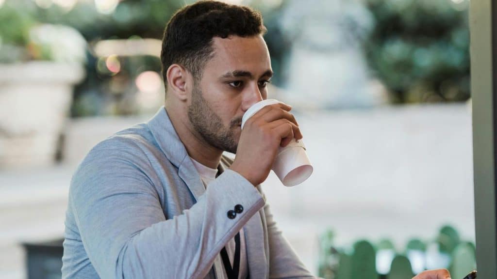A man drinking from a paper cup while sitting outdoors.