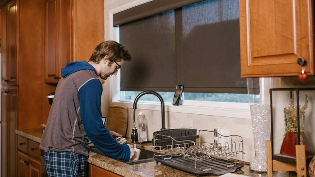 A man washing dishes in a kitchen sink.