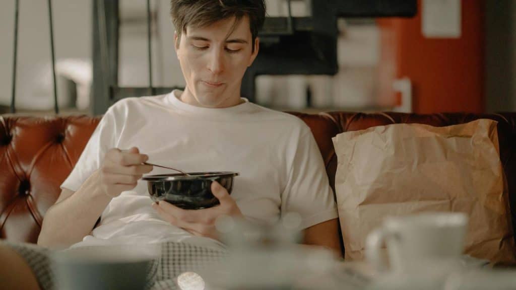 A man sitting on a couch eating from a bowl.