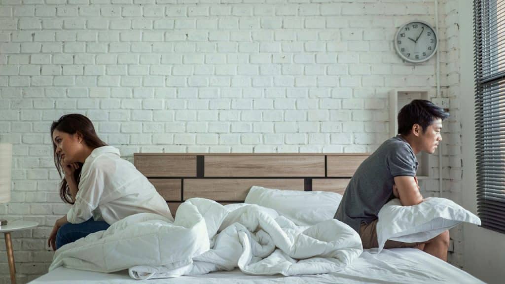 A couple sitting with their backs to each other on a bed.