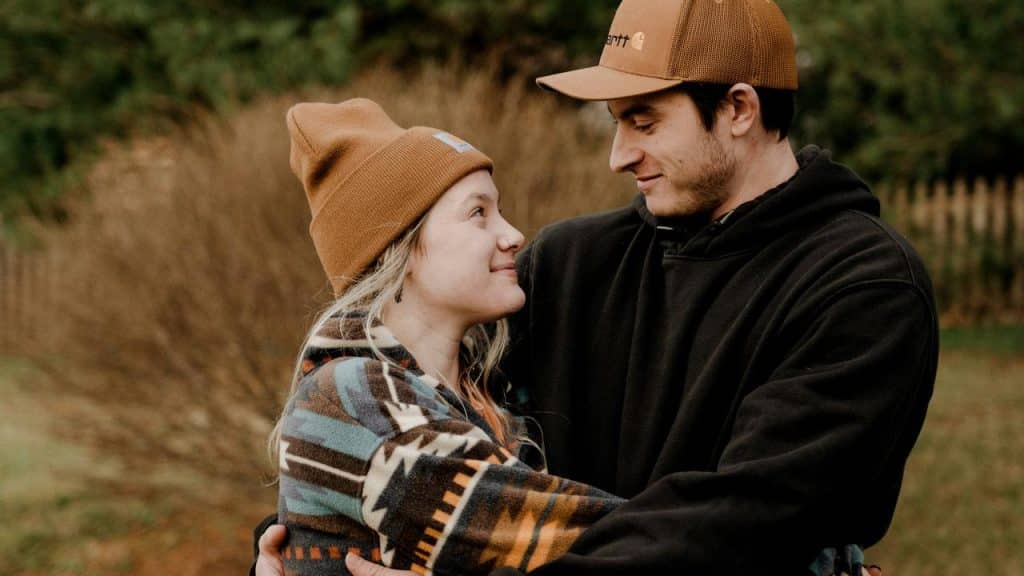A couple in cozy outdoor clothes smiling at each other while hugging.