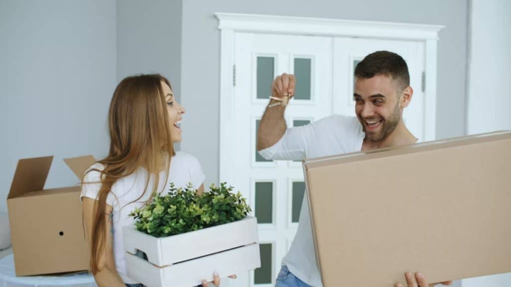 Man carrying moving boxes, smiling with his partner