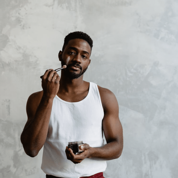 A Man in White Tank Top Applying a Face Mask on His Face Using a Brush